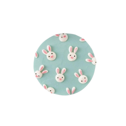 A circular dog treat cake with a light blue background and decorated with multiple small, white and pink bunny faces.