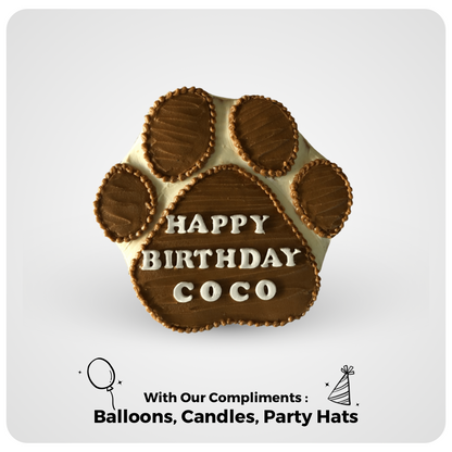 A dog birthday cake designed in the shape of a paw print with the text 'HAPPY BIRTHDAY COCO', along with illustrations of balloons, candles, and party hats.