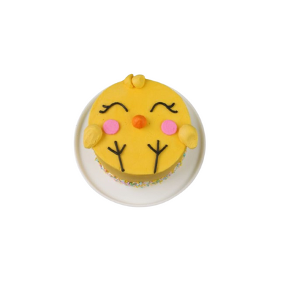 A cake designed to look like a yellow chicken with smiling face and arms, decorated with sprinkles on top.