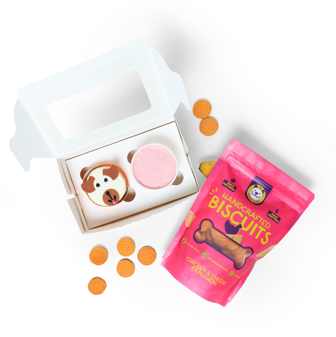 Dog treats including a pink biscuit, a box with a dog design, and a pink bag of 'Handcrafted Biscuits' on a white background.